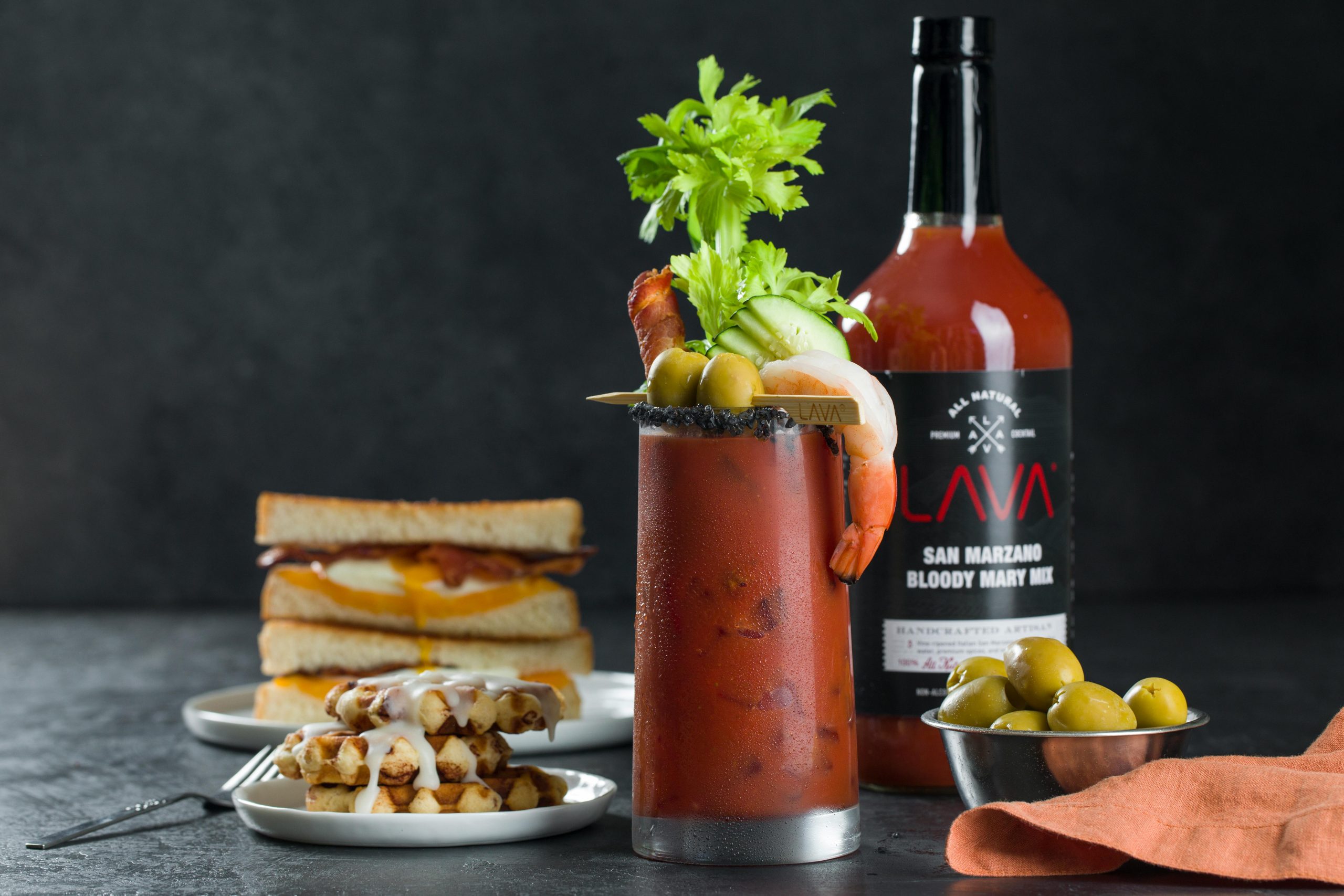 A stylish brunch setup featuring a Bloody Mary cocktail with gourmet sandwiches and waffles.