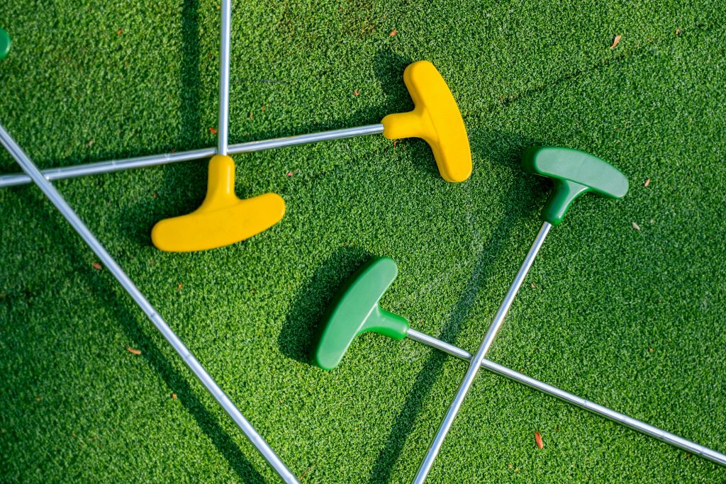 Vibrant yellow and green mini golf putters arranged on a lush green turf, perfect for leisure scenes.